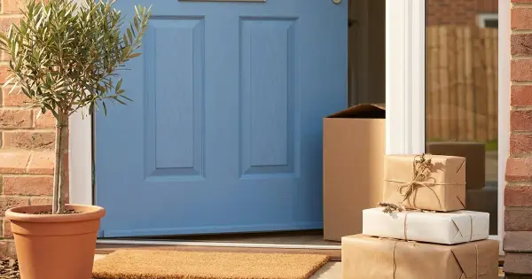 A soft blue front door of a new home with a potted olive tree and a stack of kraft-wrapped housewarming gifts on the doorstep