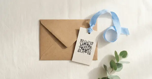 Kraft envelope with a gift tag printed with a decorative QR-style pattern and a blue ribbon on warm linen
